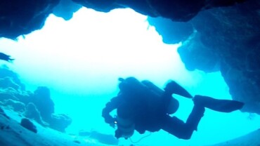 a diver swimming out of a small cave in the ocean