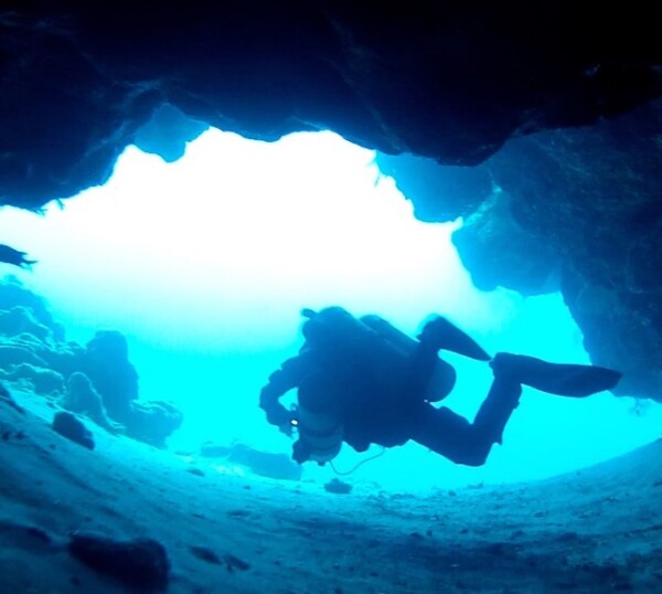 a diver swimming out of a small cave in the ocean